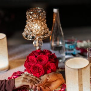 Couple holding hands at a romantic dinner with red roses and candlelight.